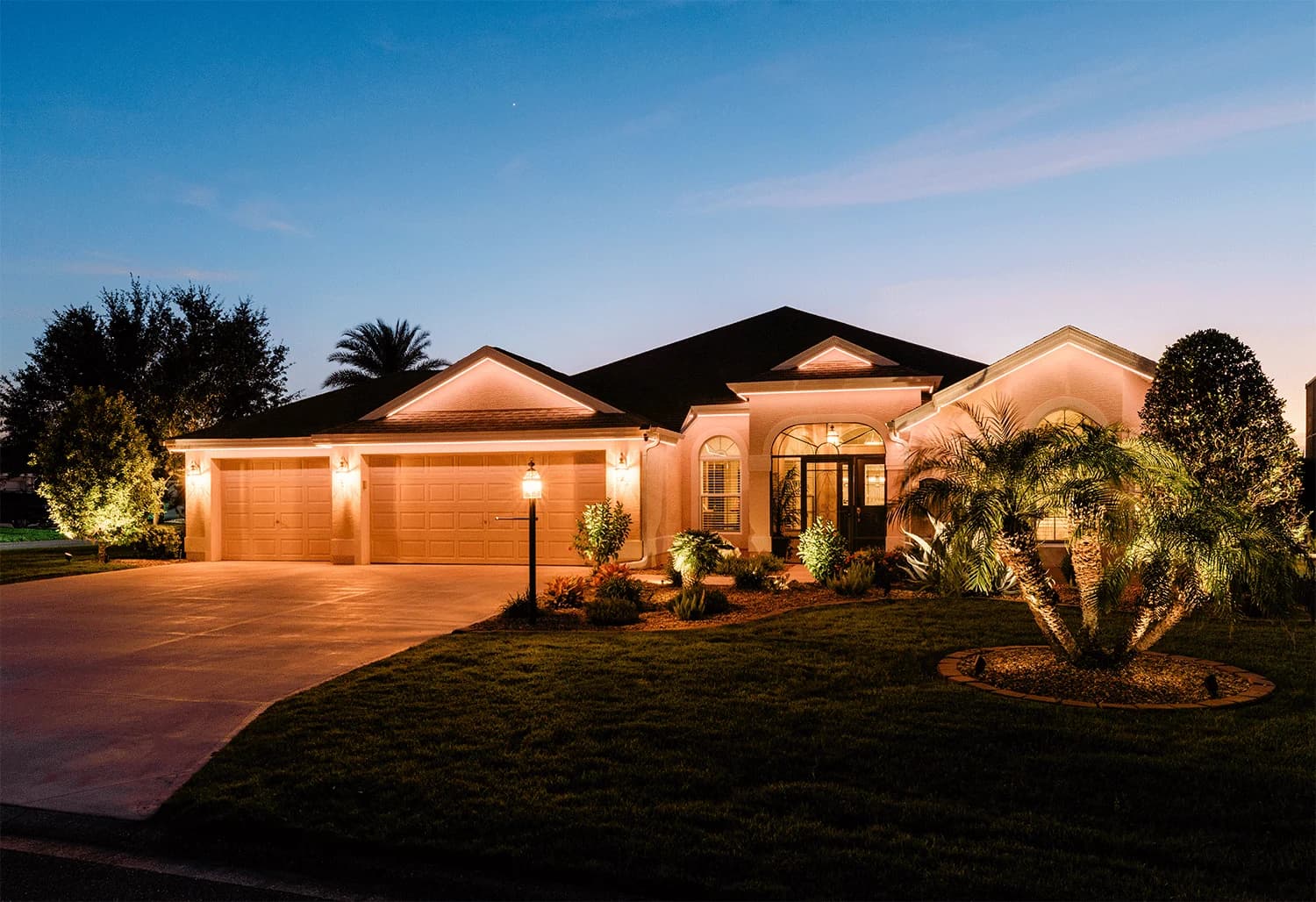 The same home at dusk with permanent roofline and landscape lighting glowing warm white